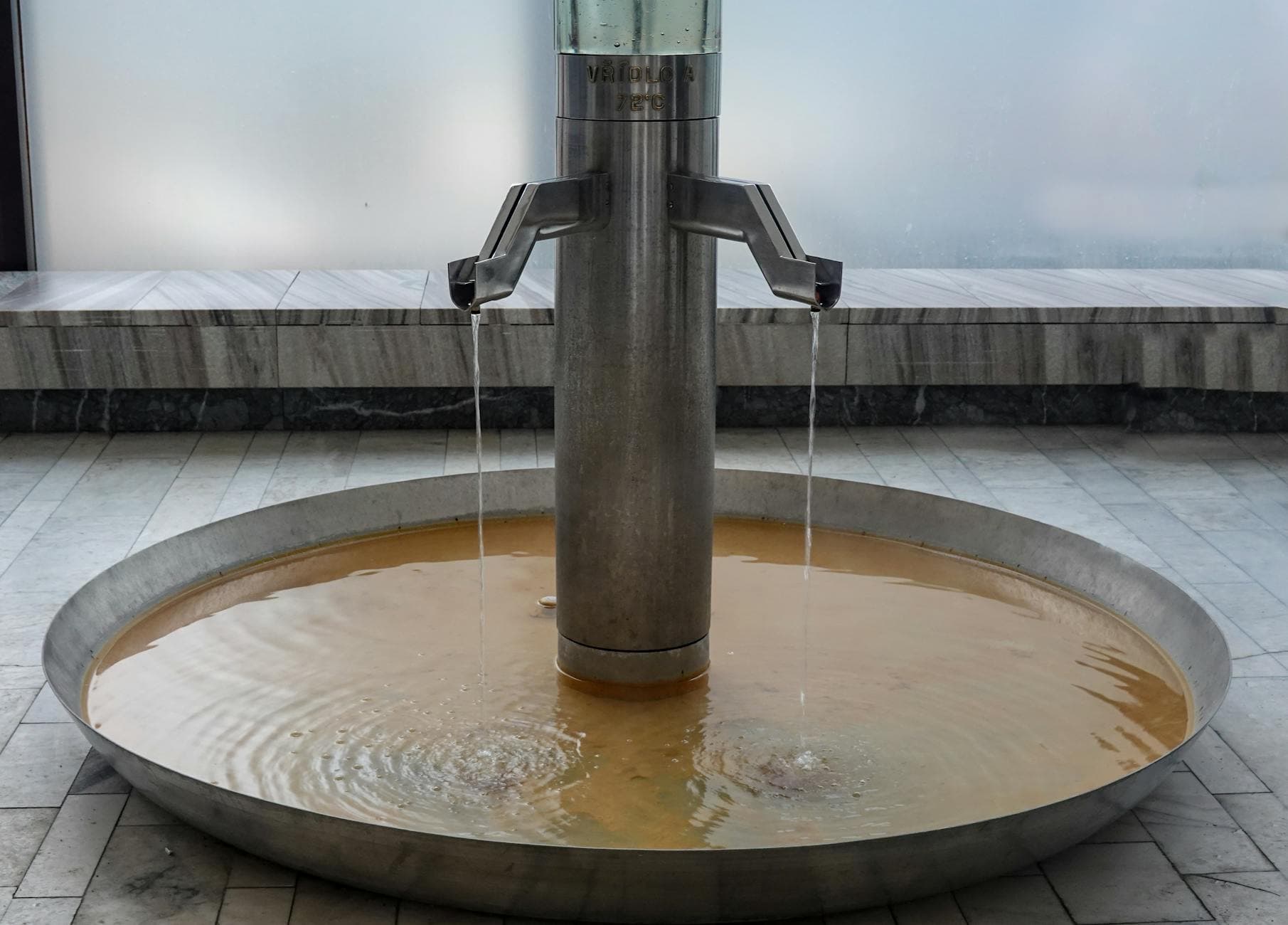 Close-up of a modern metal fountain in Karlovy Vary spa, Czech Republic, showcasing flowing thermal water.