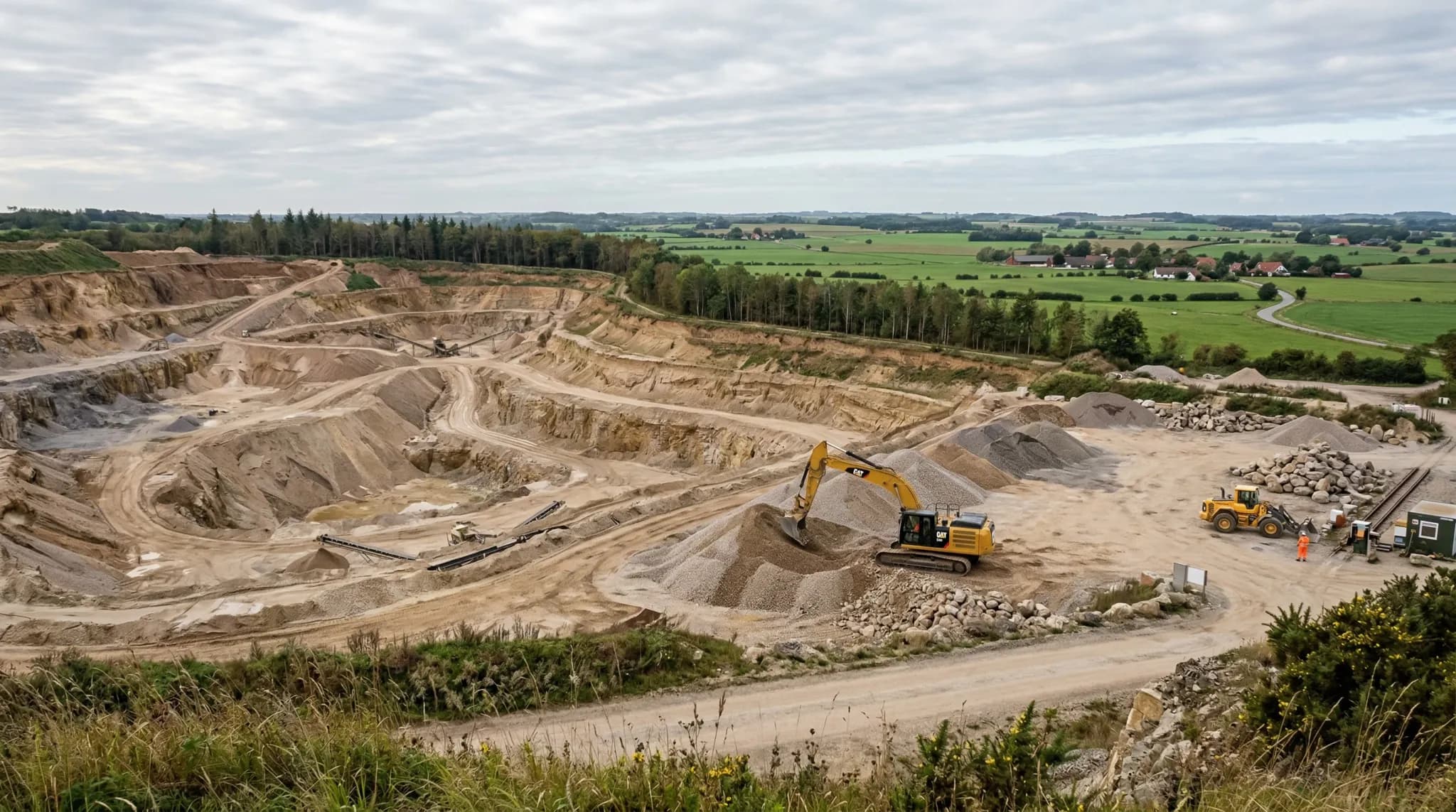 A wide-angle photorealistic shot of a large open-pit gravel quarry in the Northern European countryside. The scene shows terraced layers of sand and light brown gravel under a soft, overcast sky. In t