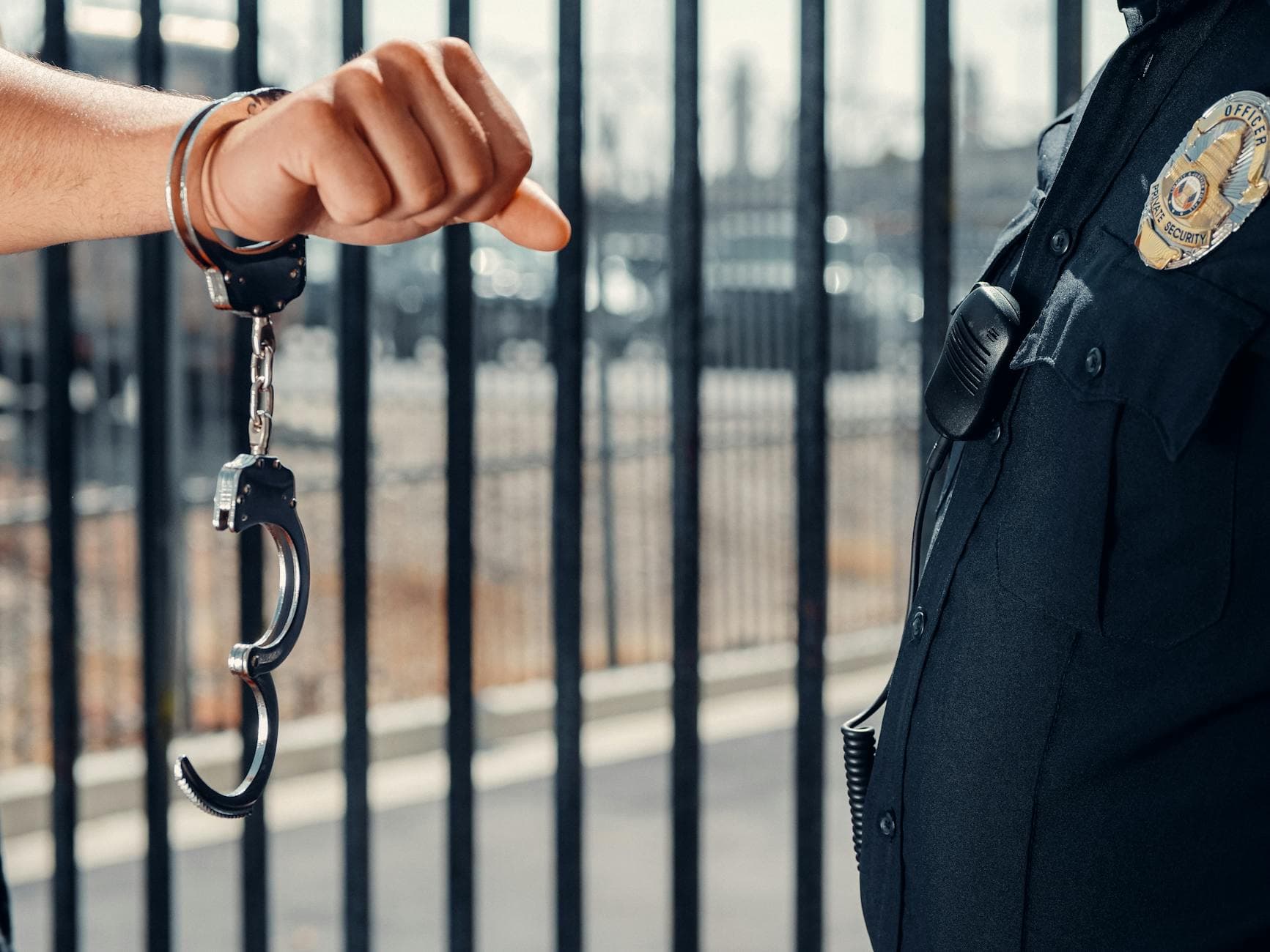 Close-up of a police officer handcuffing an individual against a metal fence outdoors.