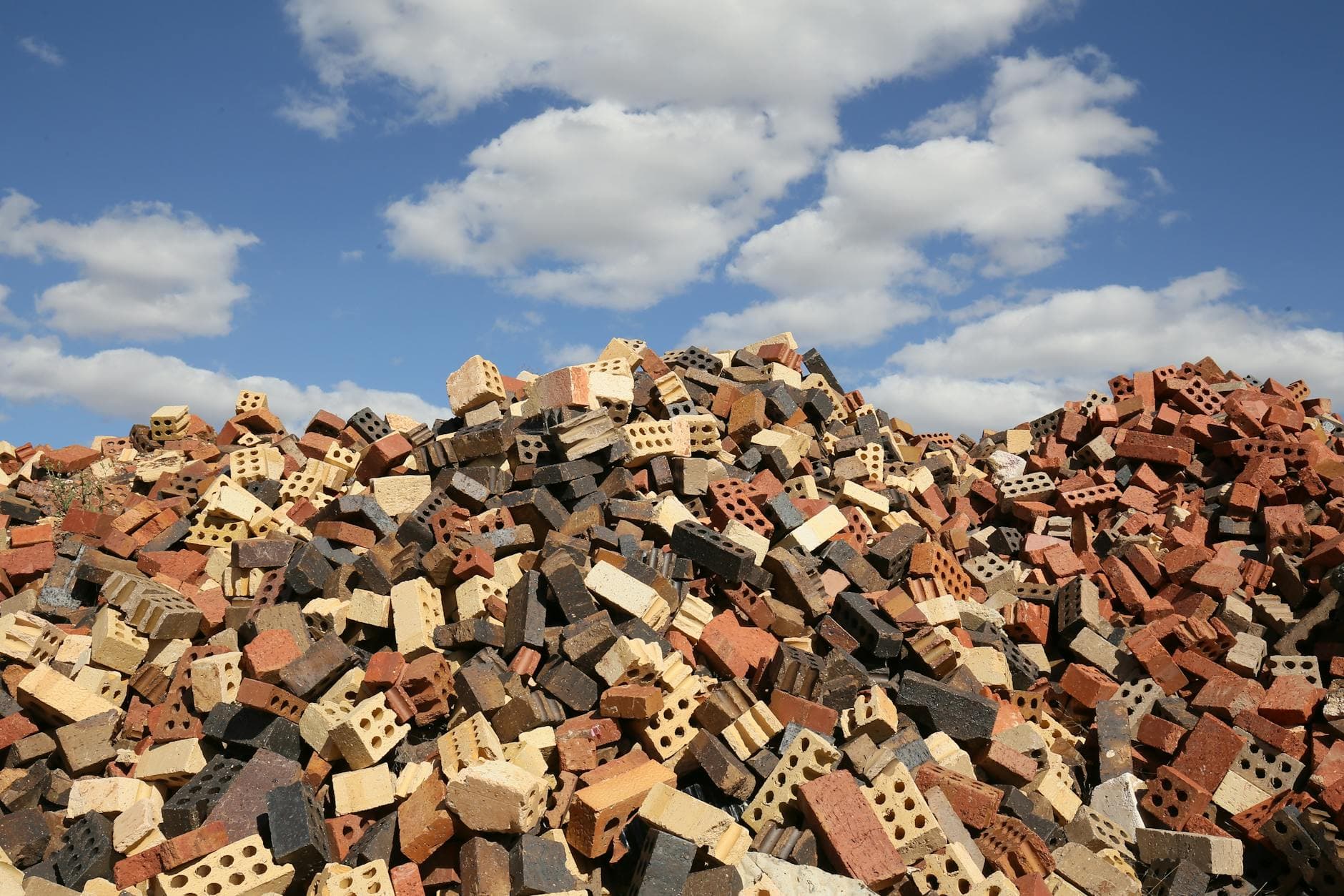 A large pile of bricks against a bright blue sky with scattered white clouds.
