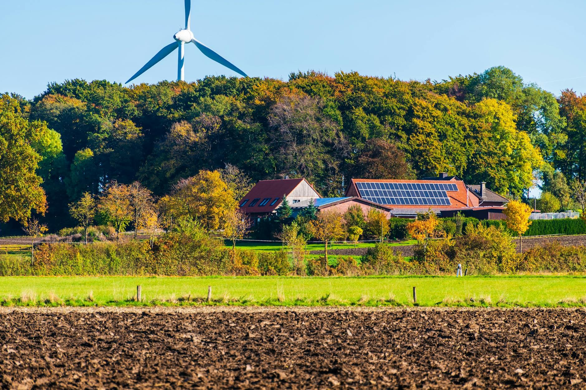 A picturesque sustainable farm featuring wind turbine and solar panels surrounded by vibrant autumn foliage.