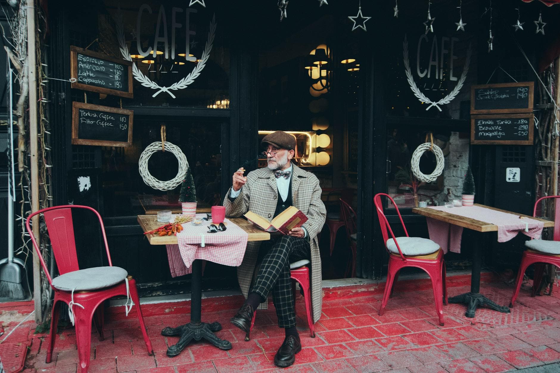 An elegantly dressed man with a book and coffee at a charming outdoor café in Istanbul, Türkiye.